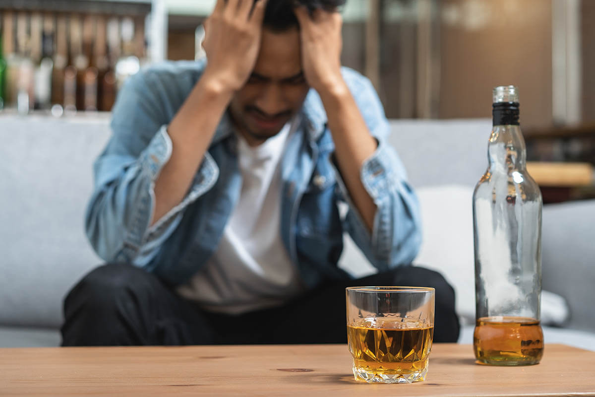 man with hands to face with alcohol on table, is alcohol a drug