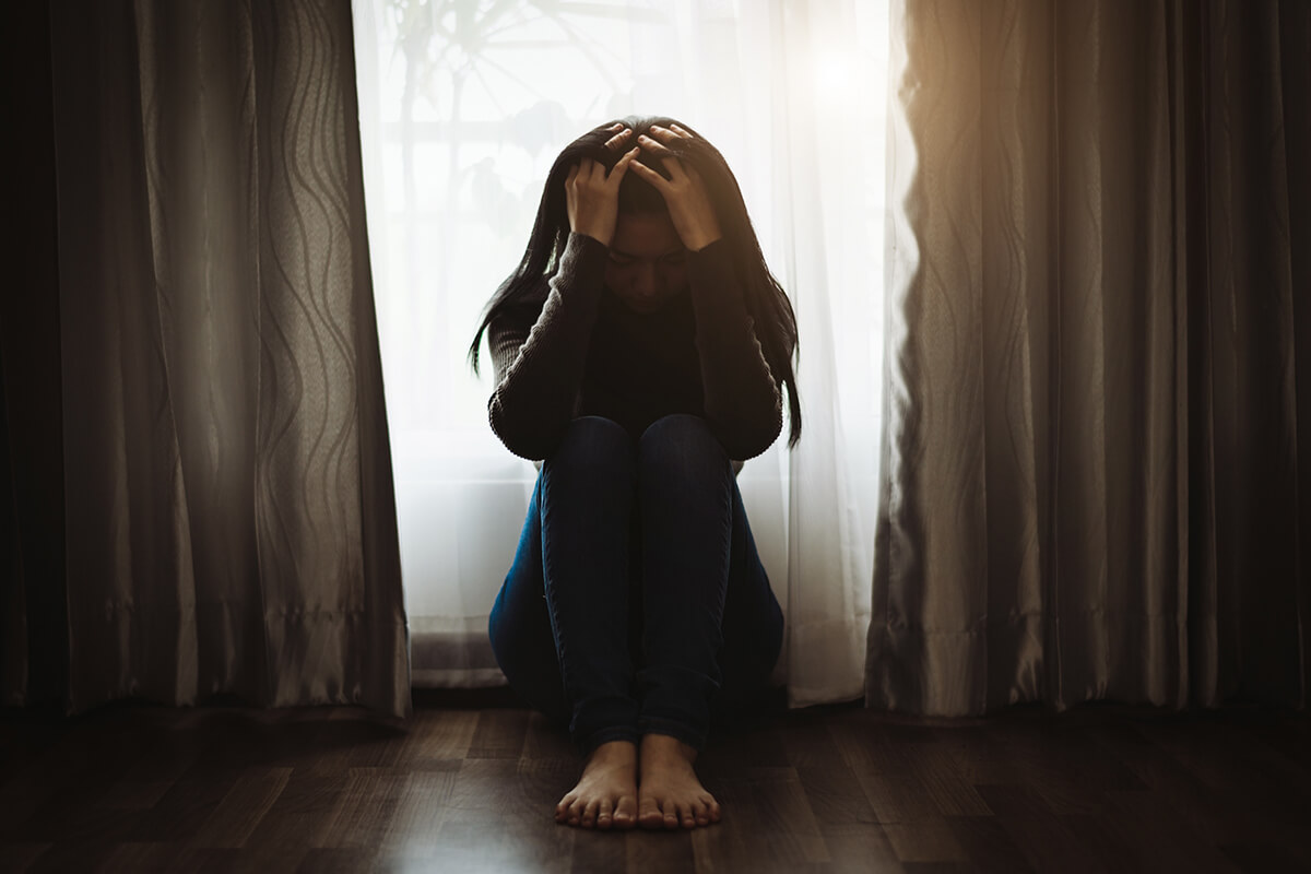 woman sitting on the floor covering her head dealing with Drug Withdrawal Symptoms