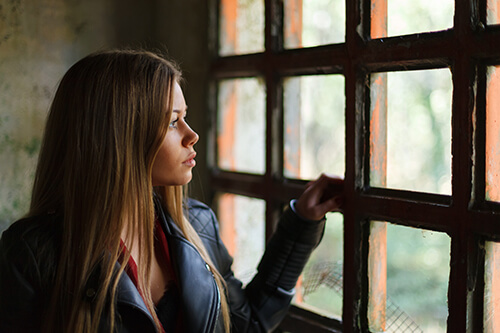 Pensive woman looking out window wondering about San Antonio addiction programs