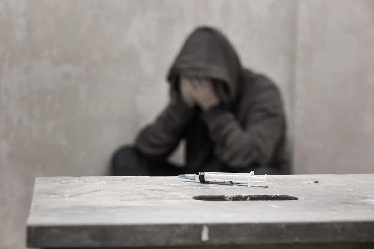 man has his head in his hands and a needle in front of him as he is a victim of the heroin epidemic