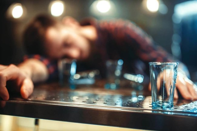 alcohol overdose symptoms, man passed out on table with several shot glasses