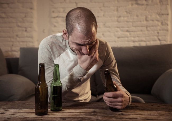 man holding his mouth looking at beer bottle suffering from alcohol addiction