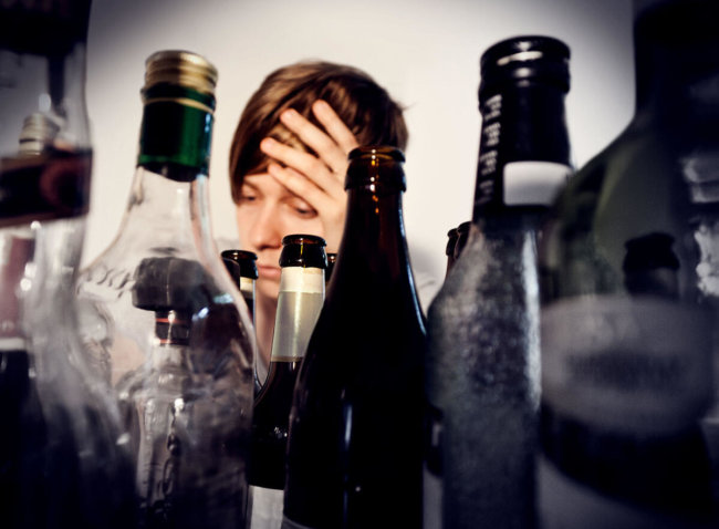 androgynous person surrounded by empty bottles of alcohol suffering from alcohol withdrawal