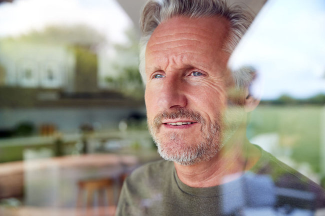older man looking out a window thinking about drug treatment centers