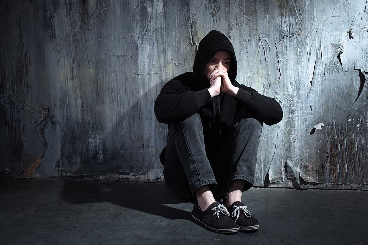 man in a hoodie slumped against a wall wondering is addiction a disease