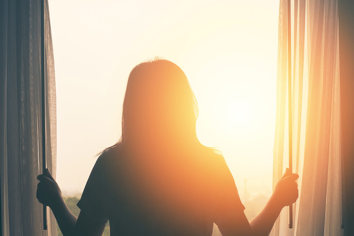 woman opening up the curtains at sunrise thinking about relapse prevention