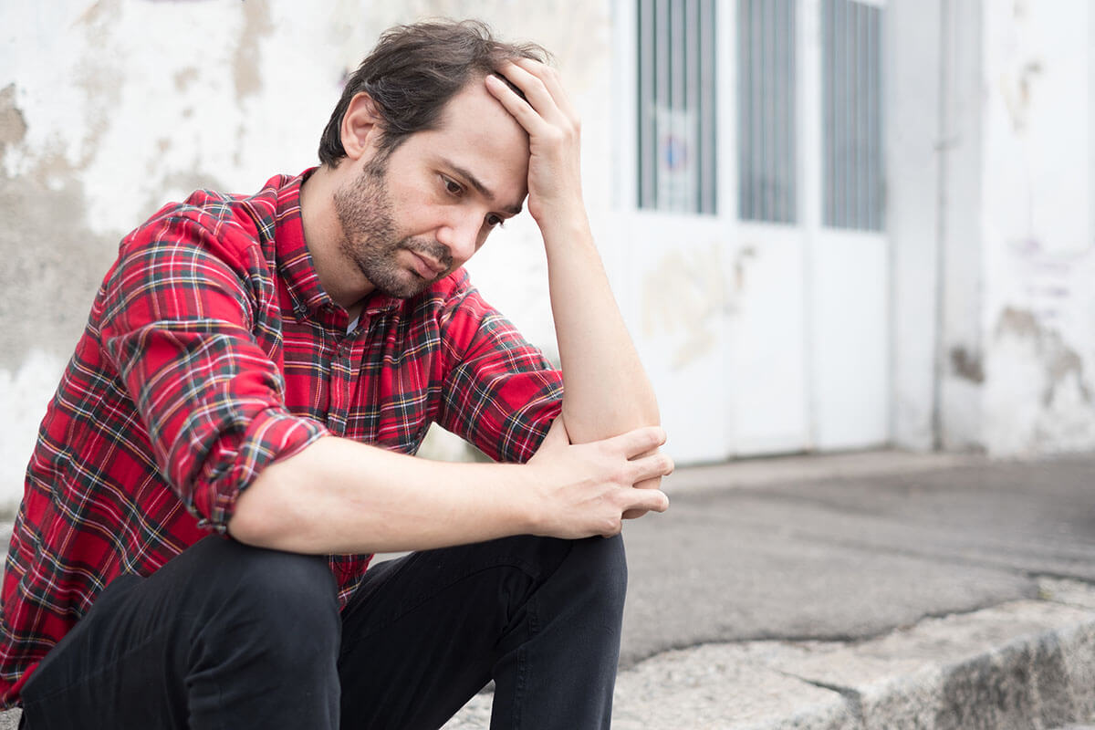 distressed flannel man sitting on a curb thinking about common mental health disorders