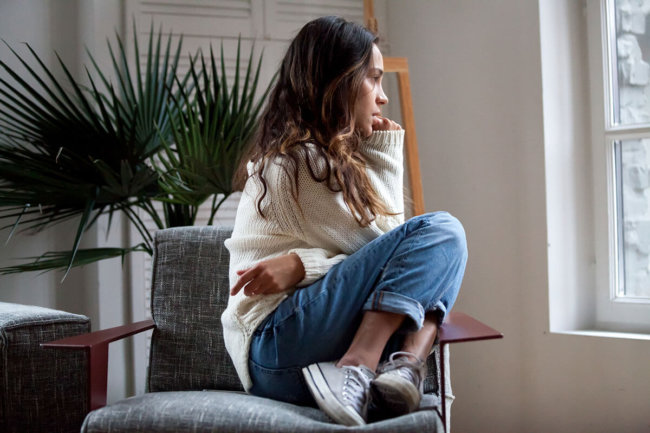 pensive woman curled up in chair exhibiting signs of drug addiction
