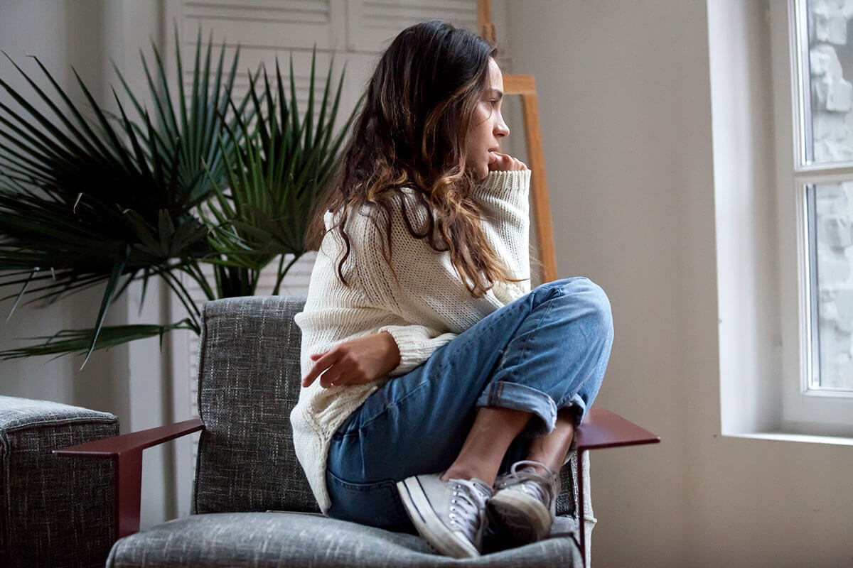 pensive woman curled up in chair exhibiting signs of drug addiction