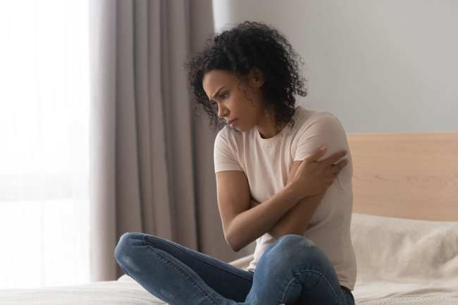 distressed woman sitting on a bed wondering what are relapse triggers