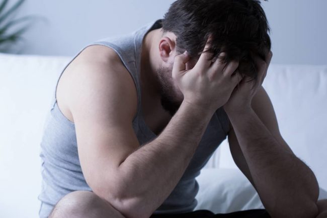a man sits on his bed with his head in his hands as he thinks about depression and anxiety